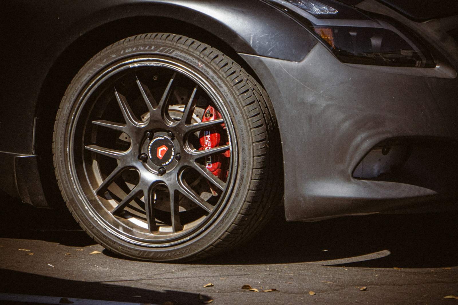 Roda de carro escuro com pinça de freio vermelha.